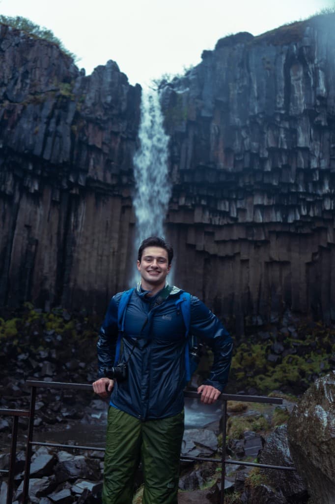 Hiker smiling in front of a basalt-column waterfall